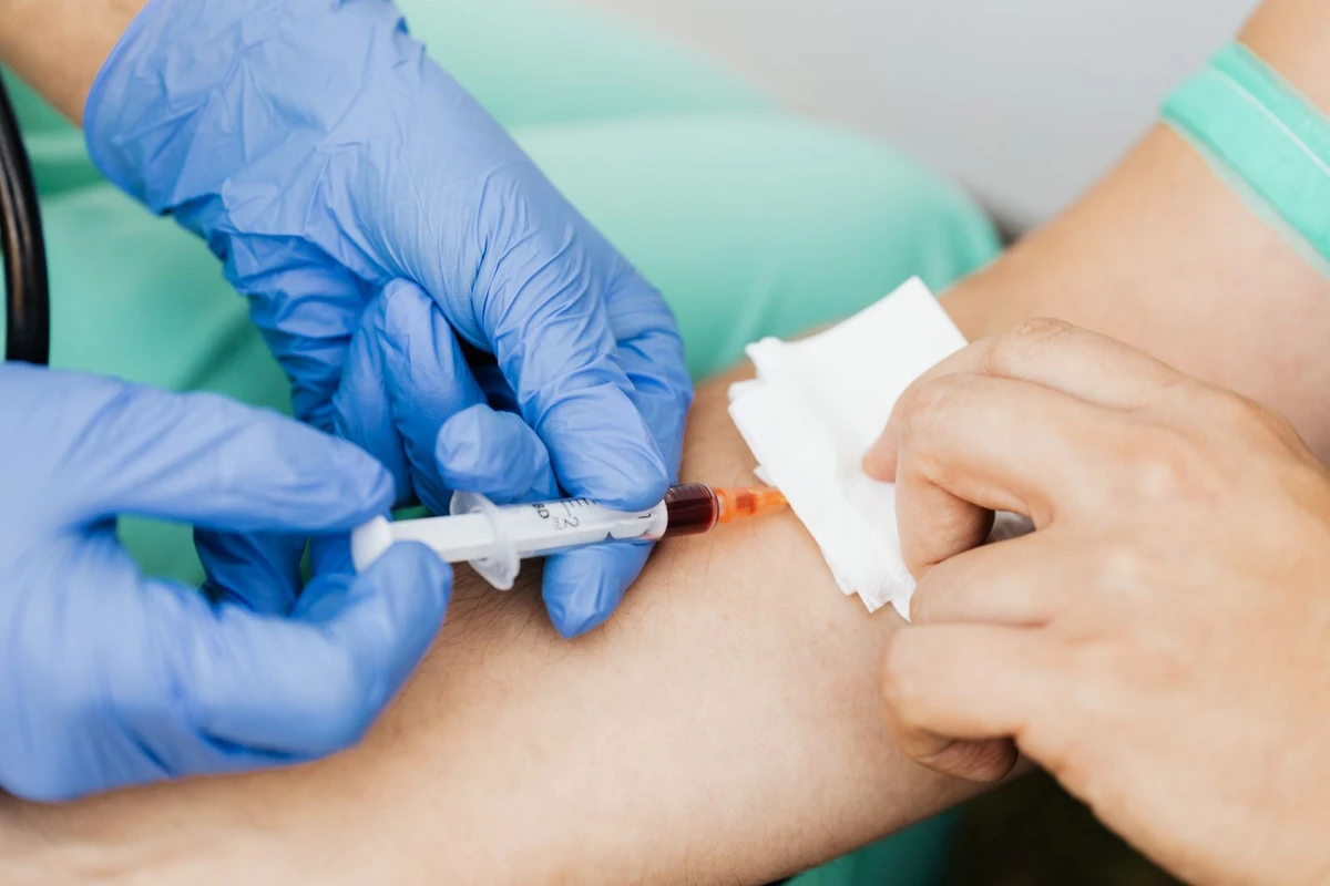 A clinician wearing gloves collects blood from a patient’s arm using a syringe